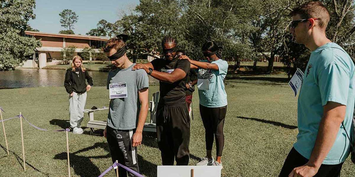 Blindfolded students stand in line with hands on the shoulders of those in front of them, waiting to walk through a maze for the Leadership Challenge event